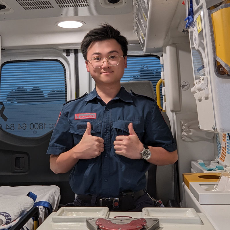 A man in Ambulance Victoria uniform gives a thumbs up to the camera from inside an ambulance