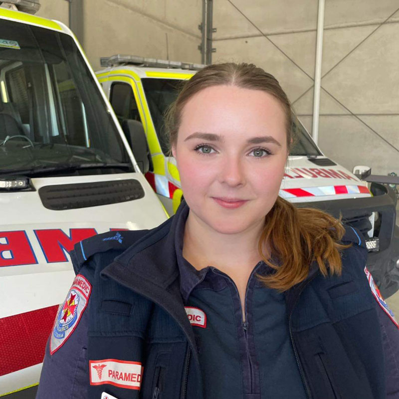 A woman in Ambulance Victoria uniform stand smiling in front of ambulances