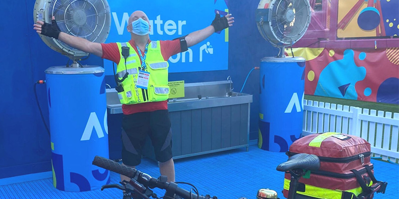 An Ambulance Victoria paramedic stands with arms outstretched in front of large fans at the Australian Open