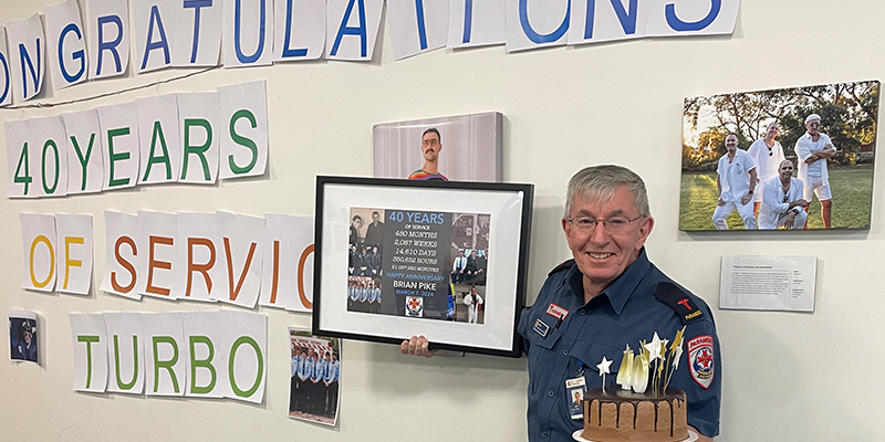 Brian Pike holding a cake and a picture frame commemorating his forty years of service with Ambulance Victoria.