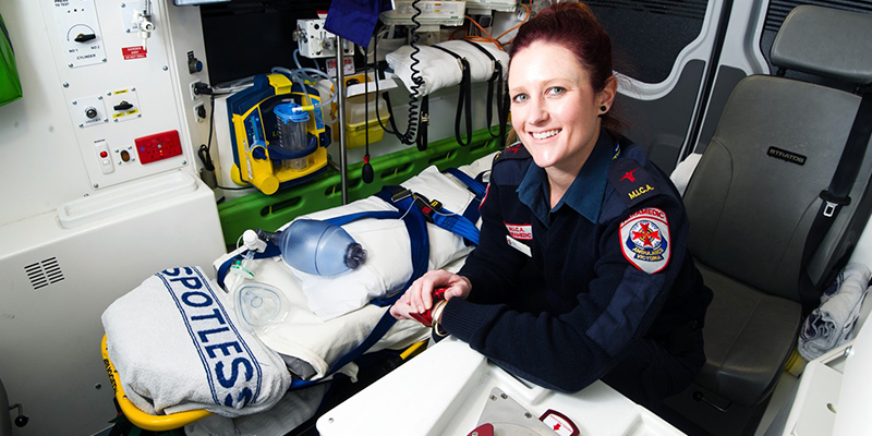 A paramedic sits beside a stretcher in an ambulance