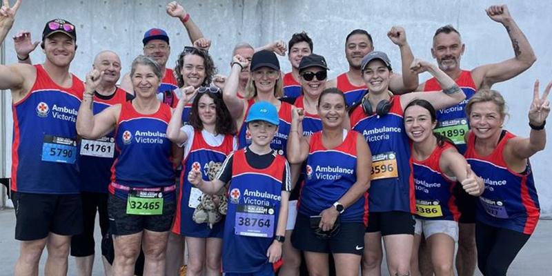 Employees of Ambulance Victoria along with their children proudly wearing the organisation's running kits and posing for a group photo.