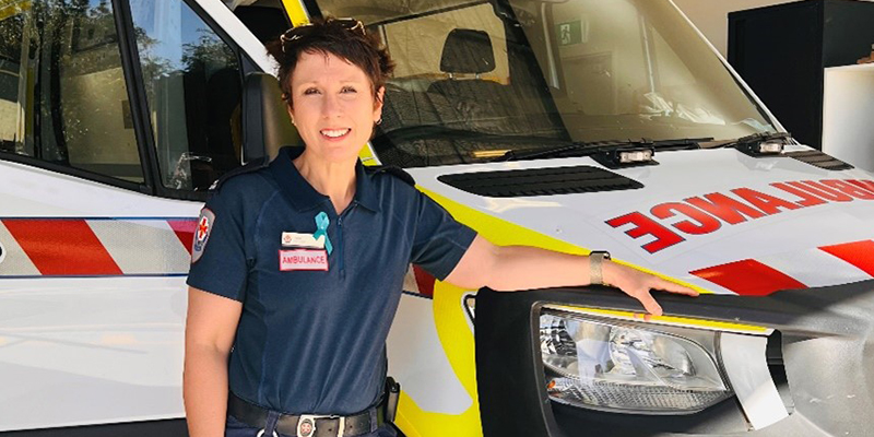 A paramedic stands beside a parked ambulance