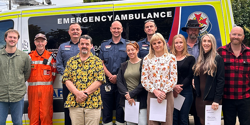 Jason is standing beside an ambulance with the group of first responder and bystanders who came to his aid.