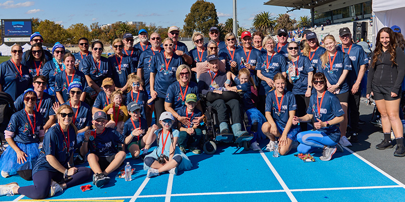 Shane is seated in a wheel chair for a group shot with many members from the Shane Swift Steppers group.