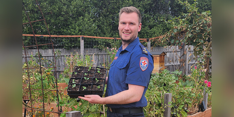 Ambulance Victoria paramedic Ash Burke is standing in his garden and holding a container with several small pots and fresh saplings growing out of the soil.