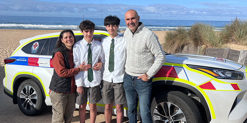 The Galiazzo family - Melina, Giordi, Gabriel and Adrian - standing beside an Ambulance Victoria vehicle parked along the beach.