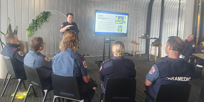 Several paramedics sitting and listening to a trainer talking about emergency scene management.